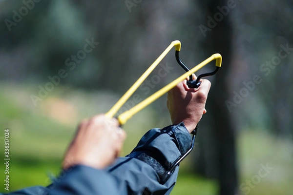 Obraz Slingshot aimed and pulled back against wrist, with hands - in forest setting