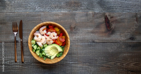 Fototapeta Healthy salad with shrimp, avocado, cucumbers, and tomatoes. Balanced lunch in bowl. Wooden background with copy space. Top view.