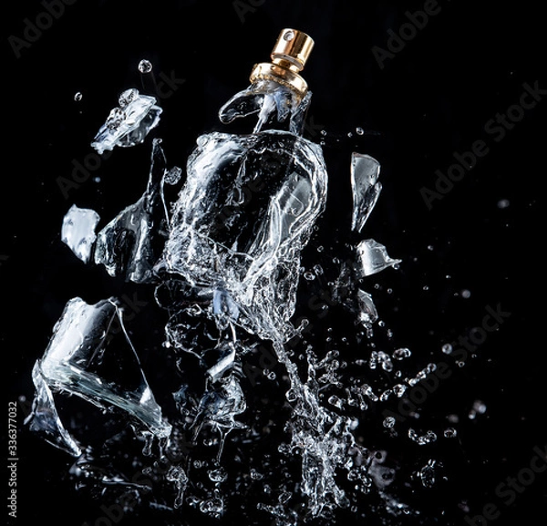 Fototapeta A glass perfume bottle shatters on a black background with splashes and drops of water