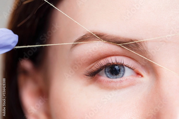 Fototapeta Cosmetologist plucks client eyebrows by thread. Close up