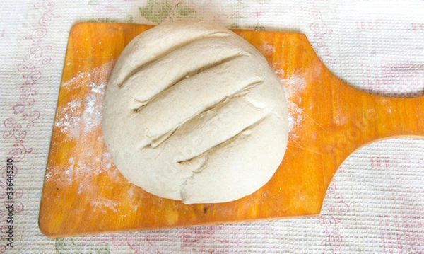 Fototapeta Preparation of dough for baking bread on a light brown wooden board and a board on a checkered white towel. Do-it-yourself baking bread at home from flour