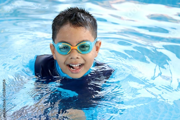 Obraz Happy child playing in blue colour swimming pool. Boy with swimming goggles. Kid practice water sport. Summer vacation concept.