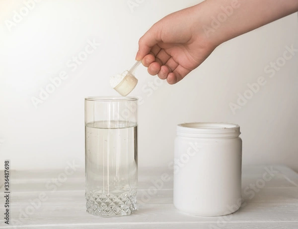 Fototapeta hand holding scoop of fish collagen. collagen peptides in container or jar. glass of water for mixing drink. Healthcare supplement concept. collagen powder for skin and joints .