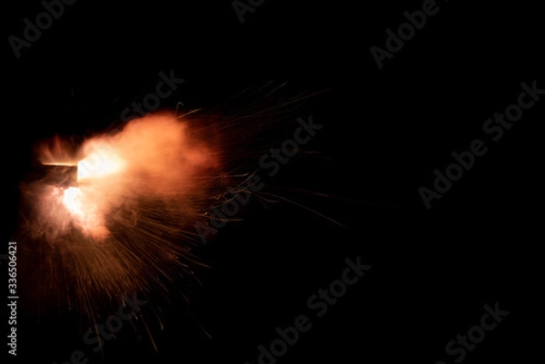 Obraz A shot from a firearm on a black background, a fiery exhaust with flying sparks, flames bursting out of the pipe