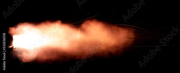 Obraz A shot from a firearm on a black background, a fiery exhaust with flying sparks, flames bursting out of the pipe