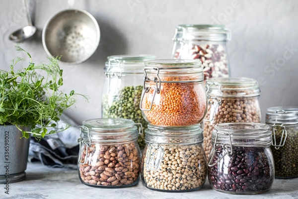 Fototapeta Set of different legumes in glass jars on, concrete white table. A source of protein for vegetarians. The concept of healthy eating and food storage.