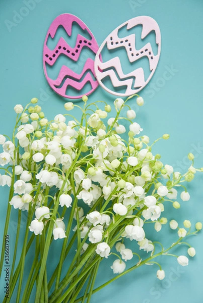 Fototapeta Floral blue background with fresh flowers. Spring greeting card for Easter. A bouquet of lily of the valley and a gift, eggs