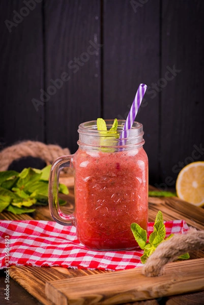 Fototapeta  fruit smoothie in a brown glass jar with a straw on a red checkered napkin on a wooden tray, juicegrated berriesberry drinkpulp juice