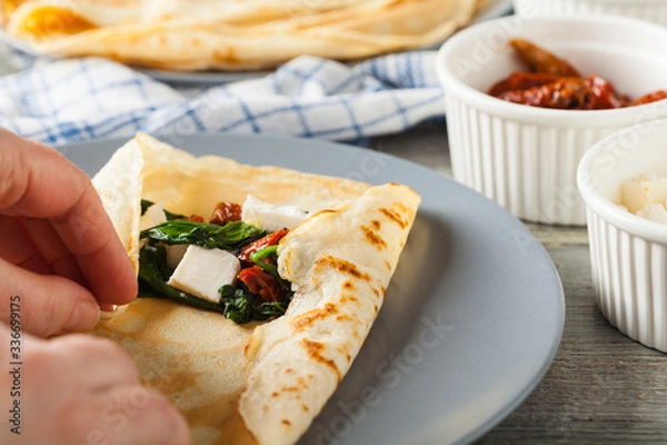 Fototapeta Pancakes with spinach, feta and dried tomatoes. Served on a gray plate. Wooden natural background.