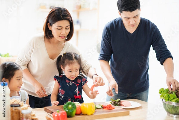 Fototapeta Young Asian love family are preparing the breakfast, sandwich vegetable on table in the kitchen which Excited smiling and felling happy. parent teach daughter to cooking food on the day at home.