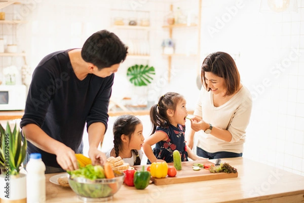 Fototapeta Young Asian love family are preparing the breakfast, sandwich vegetable on table in the kitchen which Excited smiling and felling happy. parent teach daughter to cooking food on the day at home.