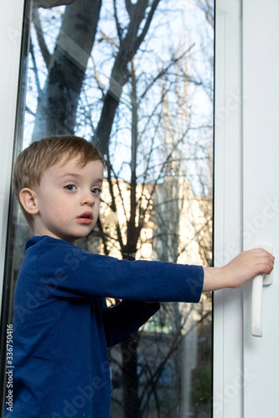 Fototapeta a small child is trying to open a window. looking at the camera
