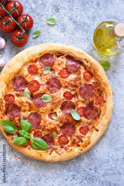 Fototapeta Salami and basil pizza. Pizza on the kitchen table, top view.