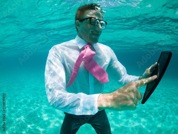 Fototapeta Businessman using a tablet computer standing under water in tropical turquoise sea