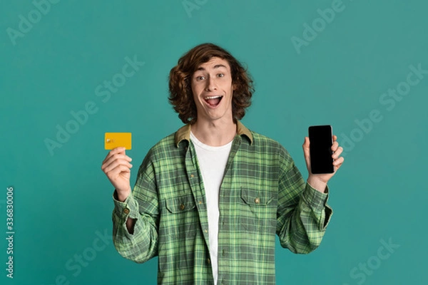 Obraz Online shopping. Happy guy holding smartphone with blank screen and credit card on color background. Space for design