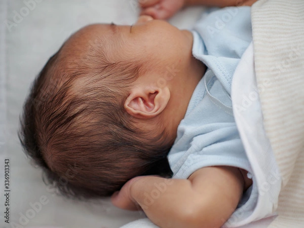Fototapeta A newborn little girl is sleeping and dreaming in her baby cot, swaddle with a warm cloth and blanket. She feels comfortable, relax, and peaceful. Selective focus on ear.