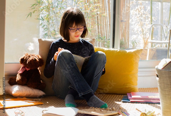 Obraz smiling child reading a book while virus lockdown, sunny balcony