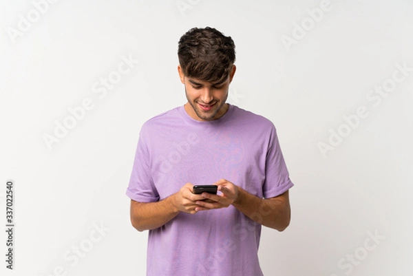 Fototapeta Young handsome man over isolated white background sending a message with the mobile