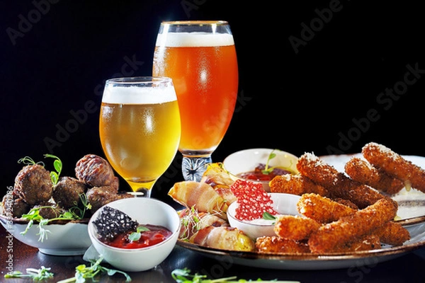 Fototapeta Beer set with lite and dark beer, sausages, red sauce, meat, lard, cheese sticks and snacks.  All products are on the table, on a black background.