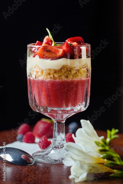 Fototapeta Delicios desert with strawberry and vanilla cream.Fresh berry with crushed nuts in glass cup.Professional and healthy food. Dessert stay close-up on a black background