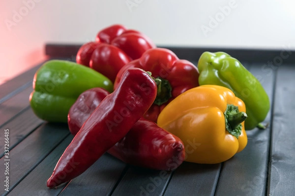 Obraz Composition of peppers of three different colors. Bright colors of vegetables. Juicy fresh peppers on a dark wooden table. Red, yellow, and green.