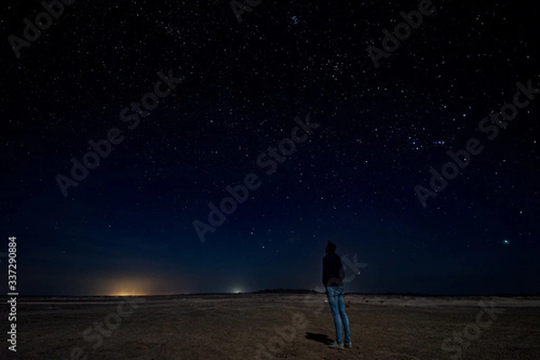 Obraz Masirah island, Oman, January 1, 2020: Gorgeous night image of a standing European man.stargazing in the middle of the desert
