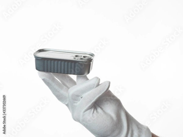 Fototapeta A man's hand dressed in a white glove holds canned food. White background.