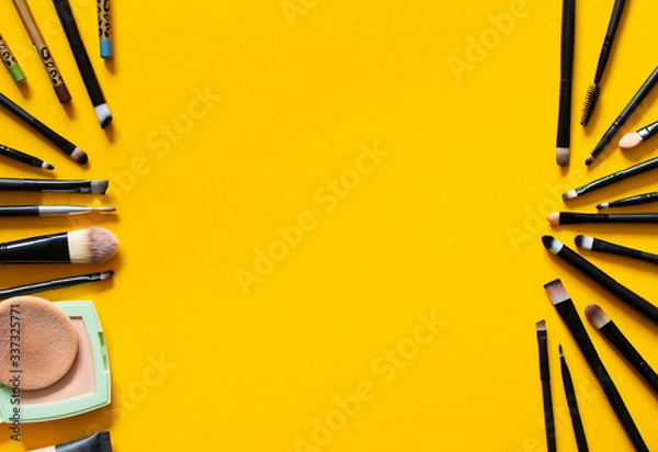Fototapeta A set of brushes for applying makeup and eye shadow to the eyelid, Foundation for the face and powder are on a yellow background, top view: design concept, make-up, beauty salon