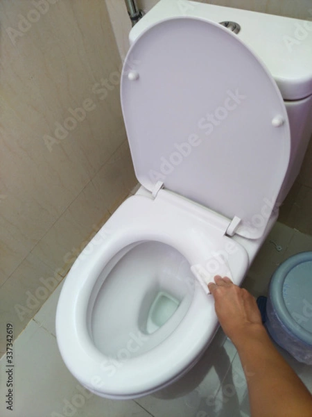 Fototapeta A man's hand uses toilet paper to wipe the toilet lid after the alcohol spray has been disinfected.