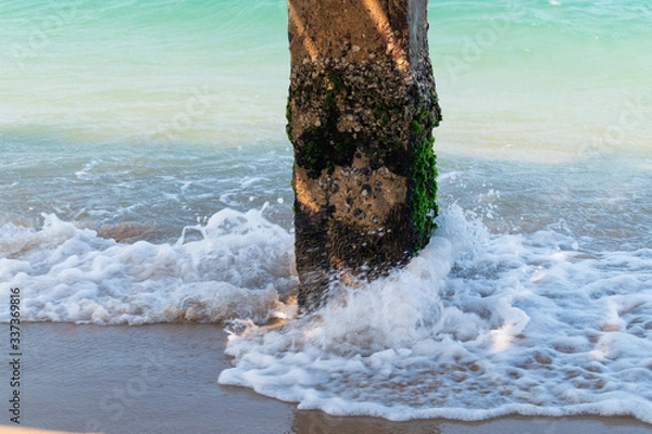 Fototapeta Concrete pillar with green moss and waves in the sea