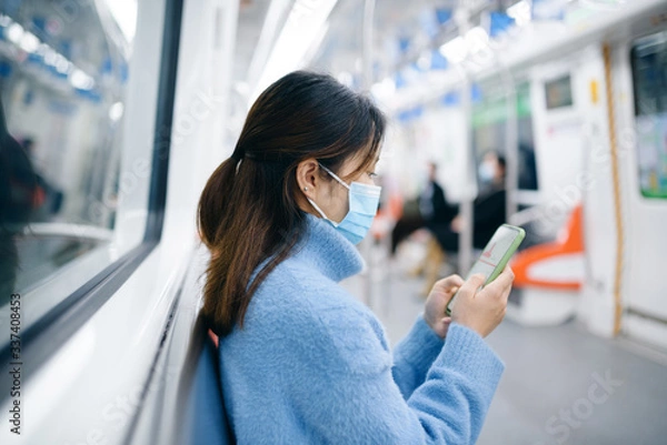 Fototapeta That young Asian woman wearing a surgical mask is using smart phone in the subway.