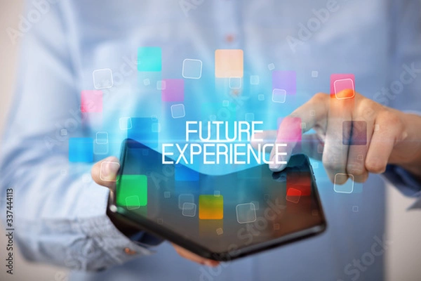 Fototapeta Young man holding a foldable smartphone with FUTURE EXPERIENCE inscription, educational concept