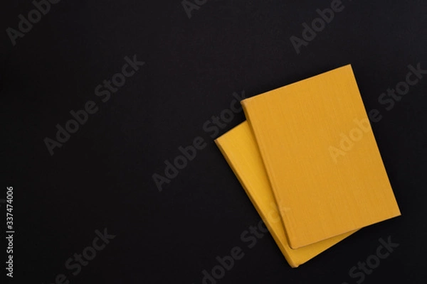 Fototapeta Two hardcover yellow books on a black background. Copy space. Dark mode style. Top view. Minimal concept