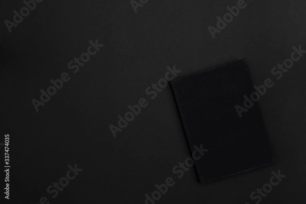Fototapeta A hardcover black book on a black background. Copy space. Dark mode style. Top view. Minimal concept