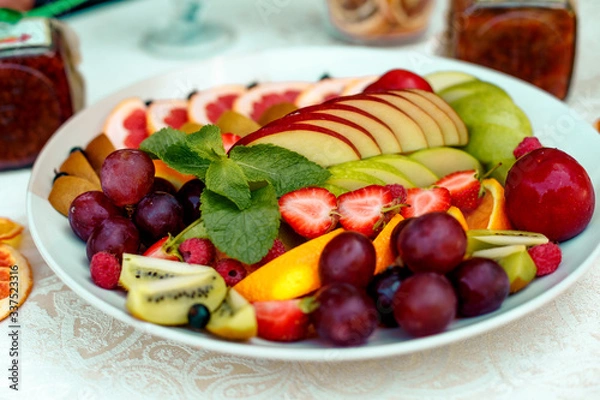 Fototapeta a plate of fruit assorted. Kiwi, grapefruit, oranges, apples, grapes and strawberries. On a white plate. Healthy food