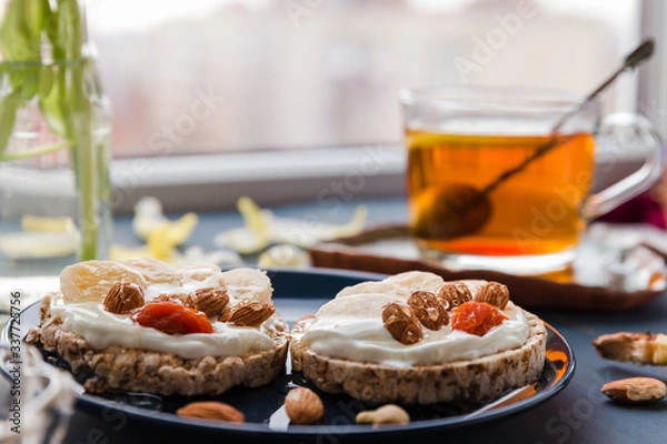 Obraz simple breakfast decoration at home. delicious toast on a blue plate. hand holding toast. breakfast at home. cup of tea with lemon and banana and almond toast. breakfast at home. breakfast idea