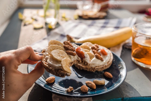 Fototapeta eating a toast on a blue plate. hand holding toast. breakfast at home. cup of tea with lemon and banana and almond toast. breakfast at home. breakfast idea. simple breakfast decoration