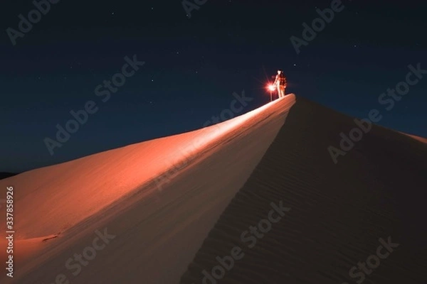 Obraz Man with red light standing on sand dune at night