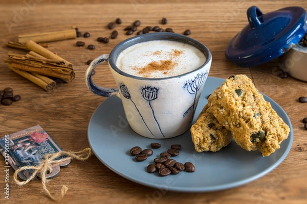 Fototapeta Cup of coffee with cinnamon sticks and cinnamon.  Rusks on a blue plate.