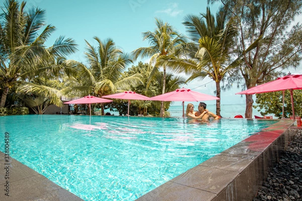 Fototapeta Para relaksująca się przy basenie otoczonym palmami z widokiem na morze na Mauritiusie