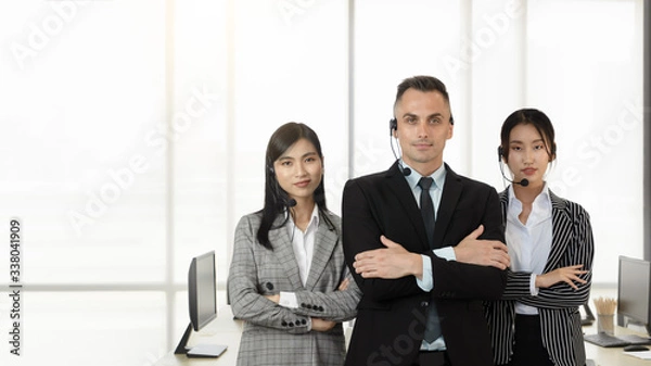 Obraz Young man and women, professional operators customer support  team with headsets standing with confidence and service mind in a call center office. Cultural diversity nationality in workplace.