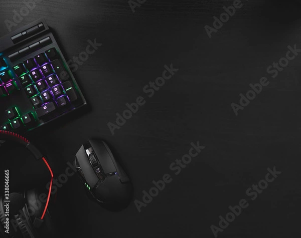 Fototapeta gamer work space concept, top view a gaming gear, mouse, keyboard, joystick, headset, mobile joystick, in ear headphone and mouse pad with rgb color on black table background.