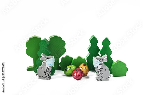 Fototapeta Easter bunnies in medical masks at a distance from each other.Wooden decoration with colorful eggs.Easter during a coronavirus pandemic.Social distance,self-isolation during the outbreak of Covid-19.