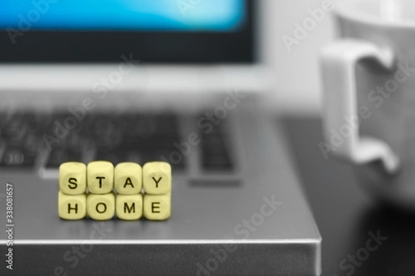Fototapeta Stay home is written by wooden cube letters with background of cup of coffee and laptop. home office concept