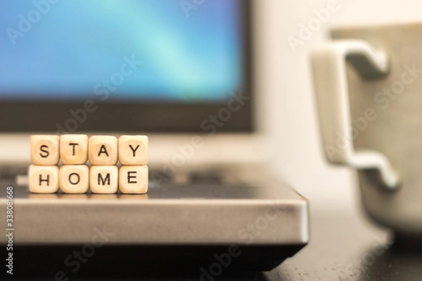 Fototapeta Stay home is written by wooden cube letters with background of cup of coffee and laptop. home office concept