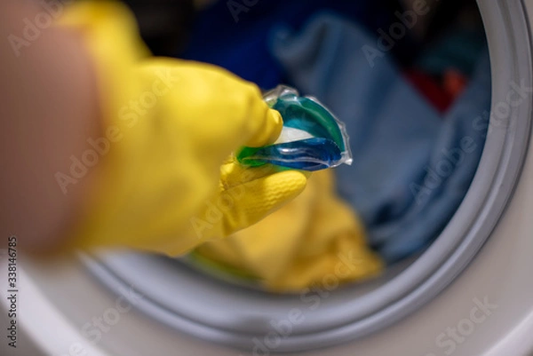 Obraz A hand in rubber glove putting a washing disc to the washing machine