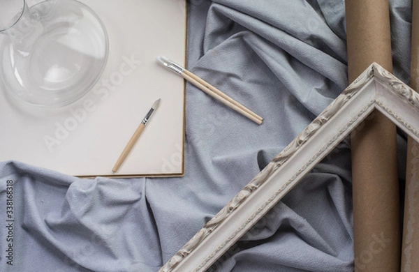 Obraz View of a creative space: brushes, vintage frame and blank paper on blue fabric.