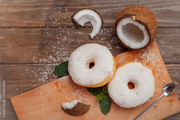 Fototapeta two large coconut donuts on a cutting board with mint leaves and coconut pieces laid out nearby
