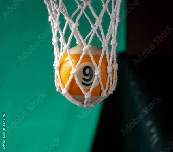Obraz In billiard pocket a ball no. nine on a green backgound.