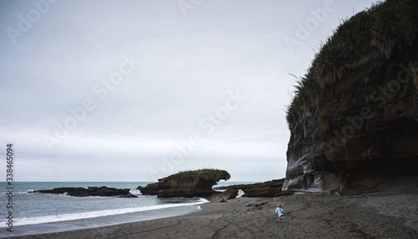 Fototapeta Gorgeous image of blonde toddler girl running down a pebbles beach taken on a cloudy winter day at Truman Track, New Zealand